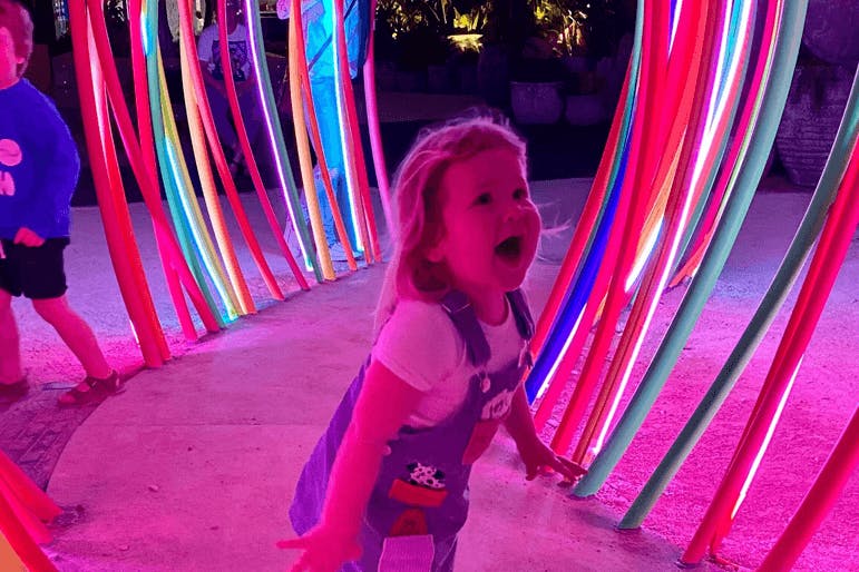 A small child playing inside a neon-lit installation.
